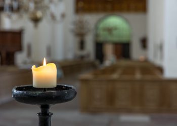 A glowing candle flame against a church interior creates a sense of deep calm, spirituality, and sacred ambiance.